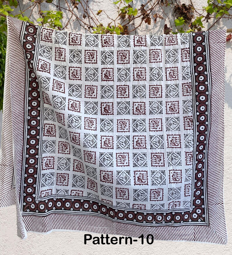 K&ouml;nnte beinhalten: Wei&szlig;er Baumwollstoff mit einem braunen und schwarzen geometrischen Muster. Der Stoff hat einen Rand mit einem sich wiederholenden Kreisdesign. Der Stoff ist mit "Pattern-10" gekennzeichnet.