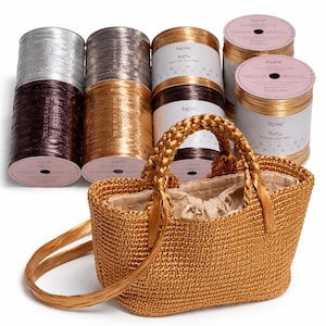 Puede incluir: Un bolso de mano de rafia tejida a ganchillo en color marrón dorado con asas trenzadas y forro de tela beige con cordón, situado frente a varios carretes cilíndricos de hilo de rafia de la marca Ispie en tonos metálicos plata, bronce y oro.