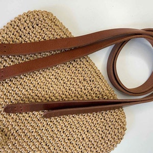 Könnte beinhalten: Eine braune gehäkelte Tasche mit zwei braunen Lederriemen. Die Riemen sind lang genug, um über die Schulter getragen zu werden.