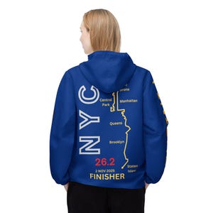 May include: A royal blue hooded jacket with white and yellow graphics. The back features the text "NYC" in white, a yellow outline of the NYC marathon route, and the text "26.2 FINISHER" in red and yellow.