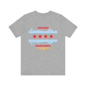 Op de afbeelding: Een grijze t-shirt met een Chicago vlag ontwerp. Het ontwerp toont de skyline van de stad, vier rode sterren en de woorden "CHICAGO MARATHON FINISHER". De shirt is gemaakt van een zacht, comfortabel materiaal.