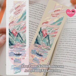 May include: A cross-stitch bookmark depicting a colourful landscape with mountains, water, and a boat. The bookmark is worked on white Aida fabric and features a pink, blue, and green colour scheme. The bookmark is labelled "Anny Funny XxStitch.etsy.com" and "Anny Funny Xxx.etsy.com".