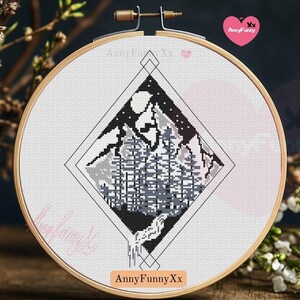 Può includere: Un ricamo a punto croce in bianco e nero di una catena montuosa con una luna e stelle nel cielo. Il motivo è a forma di diamante ed è incorniciato in un cerchio di legno. Il testo "AnnyFunnyXx" è in fondo al cerchio.