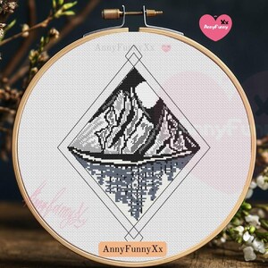 Könnte beinhalten: Schwarzweißes Kreuzstichmuster einer Bergkette mit einem Mond am Himmel, gerahmt in einem weißen Stickrahmen. Das Muster ist in Form einer Raute mit schwarzem Umriss. Der Text "AnnyFunnyXx" befindet sich am unteren Rand des Rahmens.