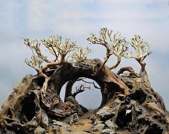 May include: A large, intricately carved wooden archway with a natural, rustic finish. The archway is decorated with several white, dried branches that create a whimsical, forest-like scene. The archway is set on a bed of sand and small rocks, creating a natural, earthy look.