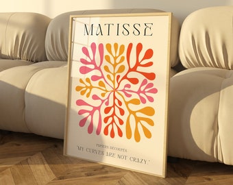 May include: A framed print with a colorful abstract design in shades of pink, orange, and yellow. The print features the text "MATISSE" and "MY CURVES ARE NOT CRAZY." The print is leaning against a white couch.