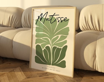 May include: A framed art print with a green abstract leaf design and the text "Matisse" and "MY COLORS ARE NOT COLD" in black. The print is in a light wood frame and is sitting on a light beige couch.
