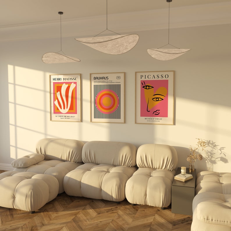 K&ouml;nnte beinhalten: Ein wei&szlig;es modulares Sofa mit drei Teilen und einem kleinen Beistelltisch. An der Wand hinter dem Sofa h&auml;ngen drei gerahmte Poster mit abstrakter Kunst. Die Poster sind mit "Henri Matisse", "Bauhaus" und "Picasso" betitelt.