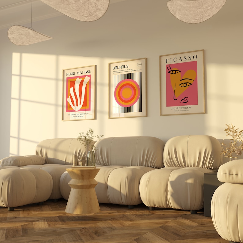 K&ouml;nnte beinhalten: Ein Wohnzimmer-Interieur mit einem beigen modularen Sofa, einem Holz-Beistelltisch und drei gerahmten Kunstdrucken an der Wand. Die Drucke zeigen abstrakte Designs in Rot, Orange, Gelb und Rosa. Die Drucke sind mit "Henri Matisse", "Bauhaus" und "Picasso" betitelt.