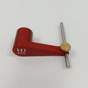 May include: A red fly tying tool with a silver rod and a gold knob. The tool has the words "HI FLY" printed on it.