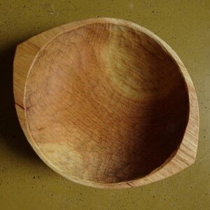 Op de afbeelding: Een handgemaakte houten kom met een natuurlijke afwerking. De kom heeft een afgeronde, ovale vorm met een platte rand. De houtnerf is zichtbaar en toont de natuurlijke kleurvariaties. Deze decoratieve kom is geschikt om te serveren of tentoon te stellen.