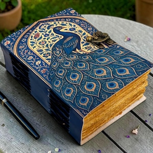 Peut inclure: Un journal décoratif avec un motif de paon sur la couverture. Le journal a une couverture bleue avec des accents dorés et un fermoir en laiton. Les pages ont une tranche dorée. Un stylo noir est posé à côté du journal sur une surface en bois.