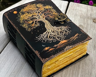 May include: A black leather journal with a gold tree of life design on the cover. The tree has intricate branches and roots, set against a starry night sky. The pages have a golden hue, and the journal is secured with a clasp.