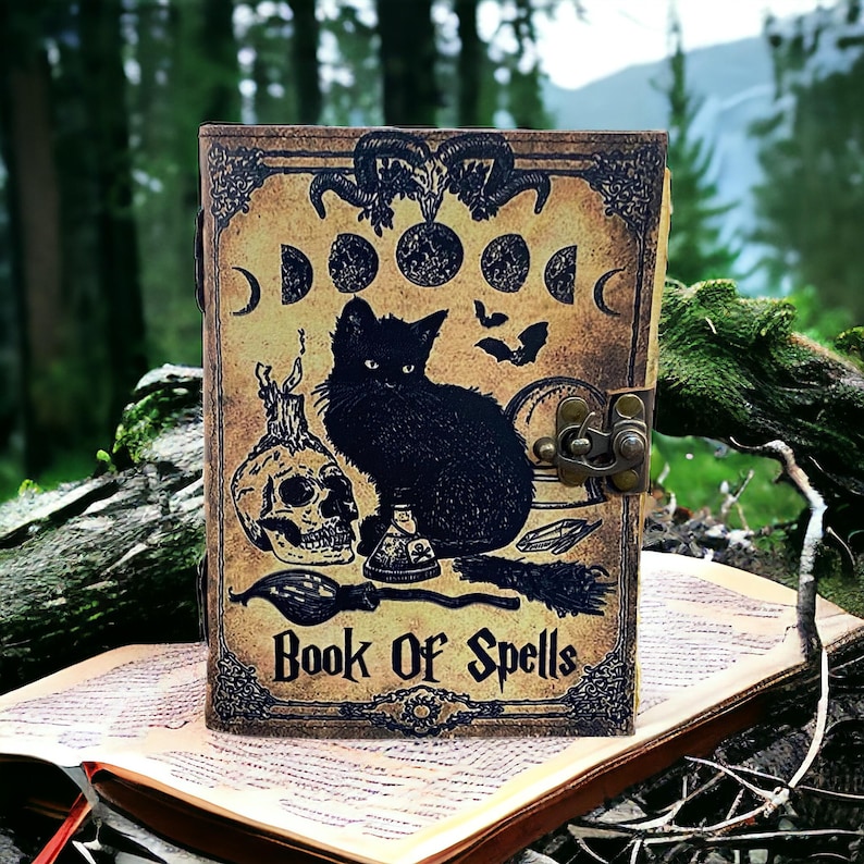 Puede incluir: Un diario de cuero marr&oacute;n con un gato negro, una calavera y otras im&aacute;genes de brujer&iacute;a. La portada dice "Book of Spells".