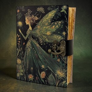 Könnte beinhalten: Ein dekoratives Notizbuch mit einer Feenillustration auf dem Einband. Der Einband zeigt einen dunklen Hintergrund mit einer Fee, die einen leuchtenden Gegenstand hält, umgeben von Blumen und Blättern. Das Notizbuch hat einen Lederriemenverschluss und gealterte Seiten.