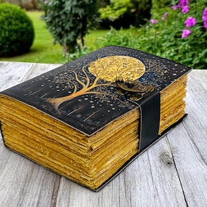 May include: A black leather-bound journal with a gold tree and moon design. The journal has a clasp closure and is made of aged paper.