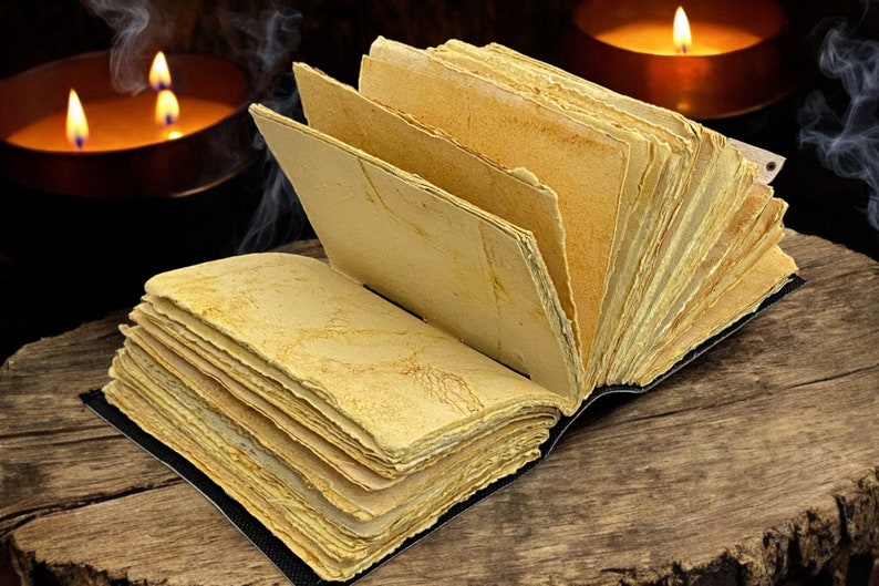May include: An open book with aged, yellowed pages and a black binding rests on a wooden surface. Two lit candles in copper holders and wisps of smoke create a mystical atmosphere in the background.