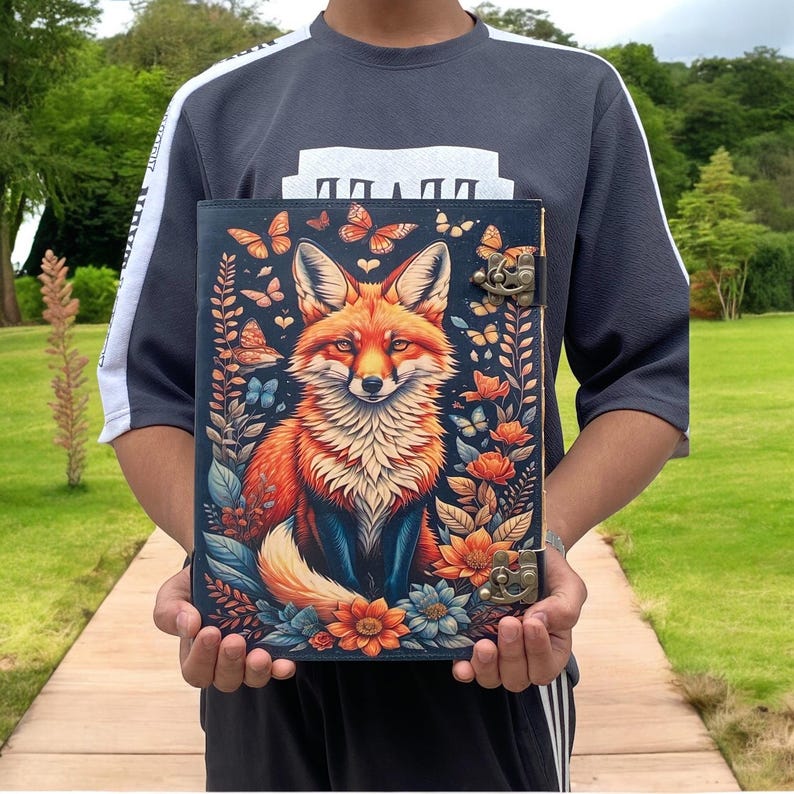 May include: A leather-bound journal with a colorful illustration of a fox surrounded by flowers and butterflies. The journal has two metal clasps and a decorative design.