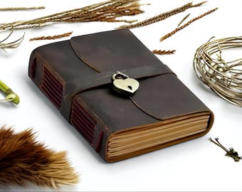 Può includere: Un diario in pelle marrone con un lucchetto a forma di cuore e una chiusura a cinturino. Il diario ha un aspetto rustico ed è perfetto per scrivere i tuoi pensieri e le tue idee.