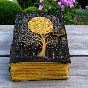 May include: A black leather journal with a gold tree and moon design. The journal has a brass lock and clasp. The pages are yellowed and have a rustic look.