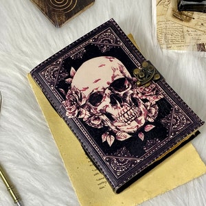K&ouml;nnte beinhalten: Ein schwarzes Lederjournal mit einem Totenkopf- und Rosenmotiv. Das Journal hat einen Messingverschluss und ist geschlossen.