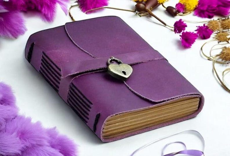 May include: A purple leather-bound journal with a heart-shaped lock and a brown wooden spine.