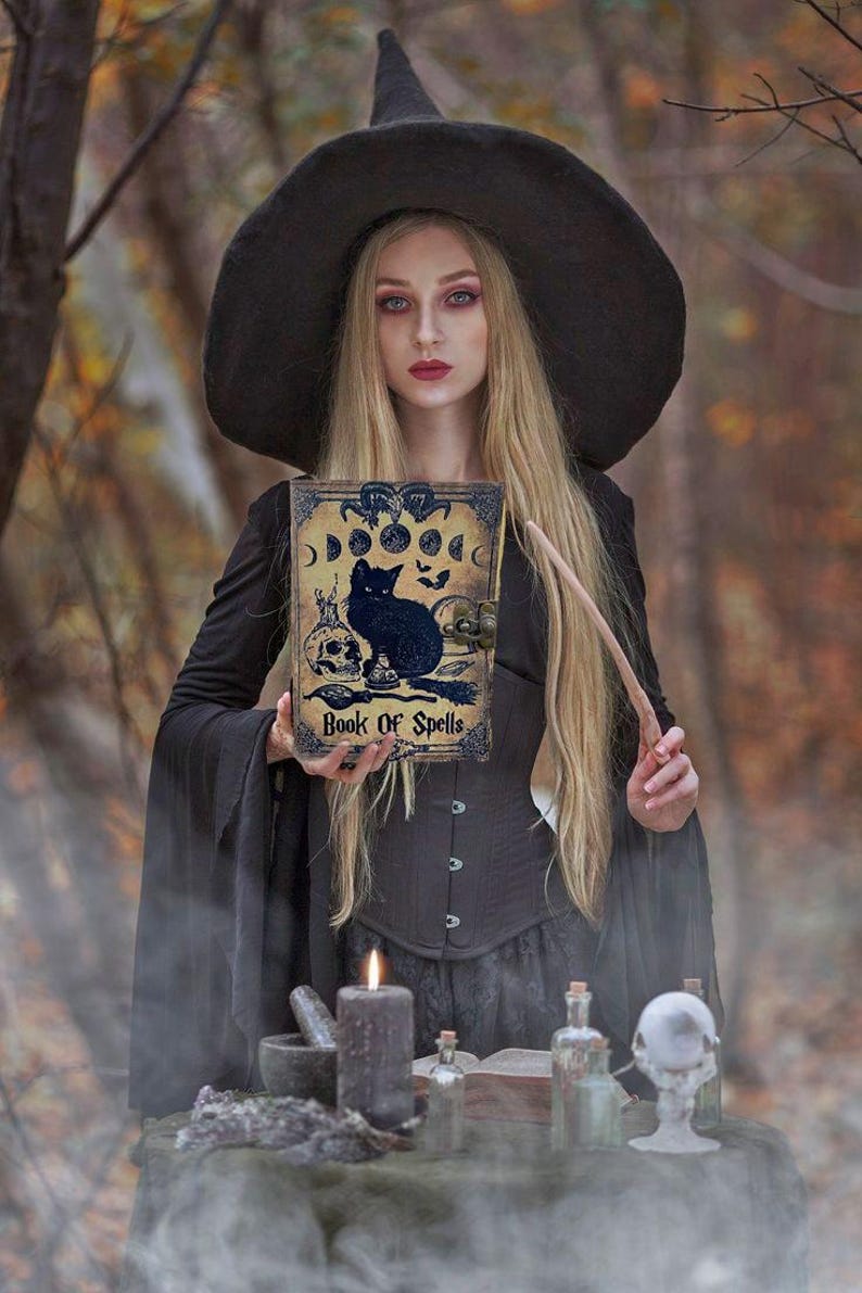 Puede incluir: Una mujer vestida de bruja sostiene un libro con un gato negro y las palabras "Book of Spells" en la portada. Est&aacute; de pie en un entorno de bosque con una mesa frente a ella, que tiene una vela, un mortero y un pil&oacute;n, y otros art&iacute;culos de brujer&iacute;a.