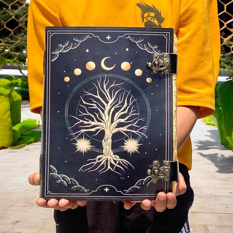 May include: A black leather journal with a gold tree of life design and a crescent moon and stars. The journal has two metal clasps.