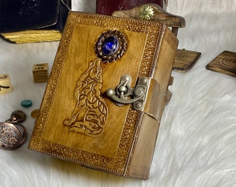 Pode incluir: Um diário de couro marrom com um design de lobo e uma pedra preciosa azul na capa. O diário tem um fecho de metal e uma borda decorativa.
