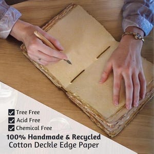 K&ouml;nnte beinhalten: Offenes handgefertigtes Baumwoll-Deckelrand-Papierjournal mit Stift. Das Journal ist baumfrei, s&auml;urefrei und chemiefrei. Das Papier hat eine hellbraune Farbe mit einem B&uuml;ttenrand. Der Text auf dem Bild lautet: 100% Handmade & Recycled Cotton Deckle Edge Paper.
