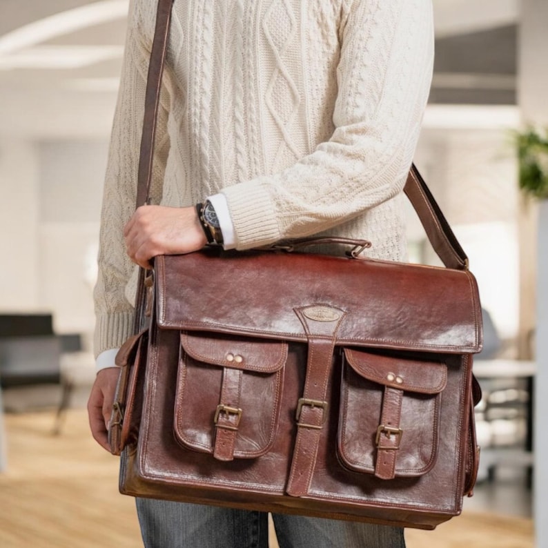 May include: A brown leather briefcase with two large front pockets and buckles. The briefcase has a long strap and is worn over the shoulder.