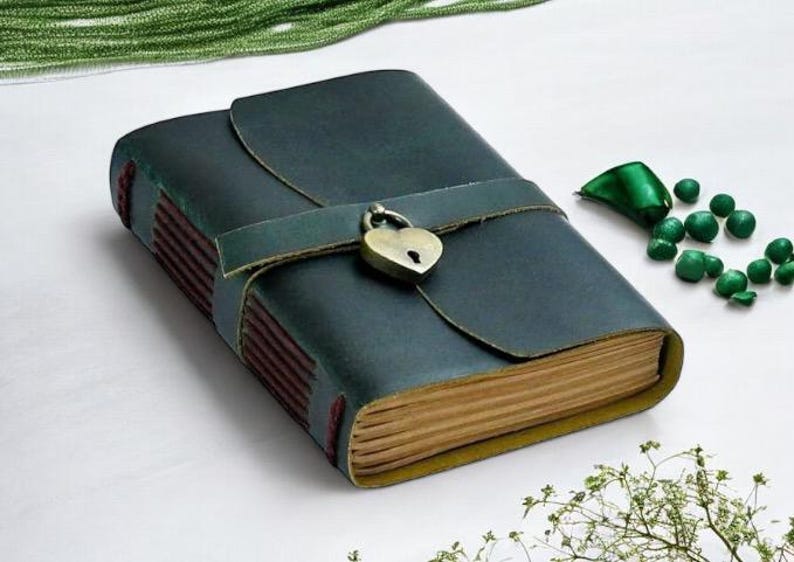 May include: A dark green leather journal with a heart-shaped lock and a brown leather strap. The journal has a rustic look and is perfect for writing down your thoughts and ideas.
