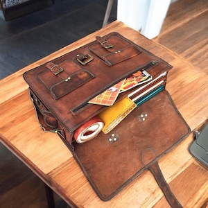 May include: A brown leather briefcase with multiple pockets and a zippered closure. The briefcase is open and has various items inside, including folders, papers, and a roll of tape.