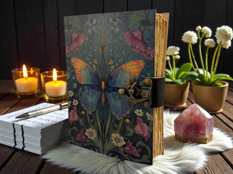 May include: A decorative journal with a butterfly design on the cover. The cover features a blue and orange butterfly with floral accents. The journal is secured with a leather strap and metal clasp. The pages have a vintage, aged appearance.