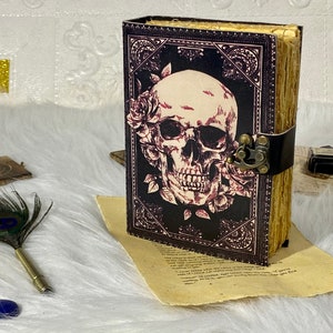 K&ouml;nnte beinhalten: Ein schwarzes, ledergebundenes Tagebuch mit einem Totenkopf- und Rosenmotiv. Das Tagebuch hat einen Metallverschluss und einen dekorativen Rand.