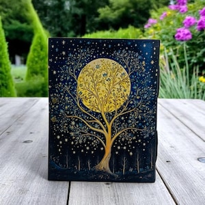 May include: A dark blue leather journal with a gold and yellow tree design. The tree is surrounded by a full moon and stars. The journal has a distressed look and is perfect for writing in.