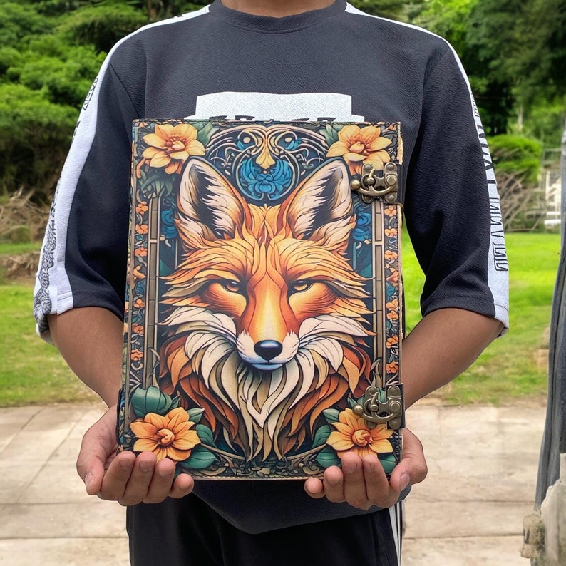 May include: A leather-bound journal with a colorful illustration of a fox surrounded by flowers. The journal has two metal clasps and a decorative design.