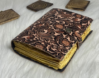 May include: A leather-bound journal with a floral pattern in black and orange on a cream background. The journal has a brass clasp and is closed.
