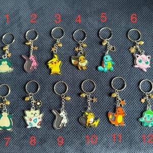 May include: Twelve keychains featuring different Pokemon characters. Each keychain has a silver ring and a charm with a different Pokemon character. The charms are made of clear plastic with colourful designs. The keychains are numbered 1 through 12.