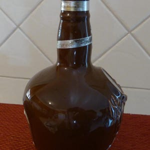 May include: A brown ceramic bottle with a silver cap. The bottle has a unique shape and a silver label with the text "Johnnie Walker" on it.
