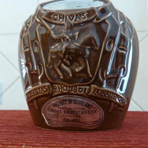 May include: A brown ceramic bottle with a label that reads "PRODUCE OF SCOTLAND BLENDED AND BOTTLED BY CHIVAS BROTHERS LTD. 750ml DISTILLERS Est. 1801 ABERDEEN SCOTLAND". The bottle has a raised design of a knight on a horse.