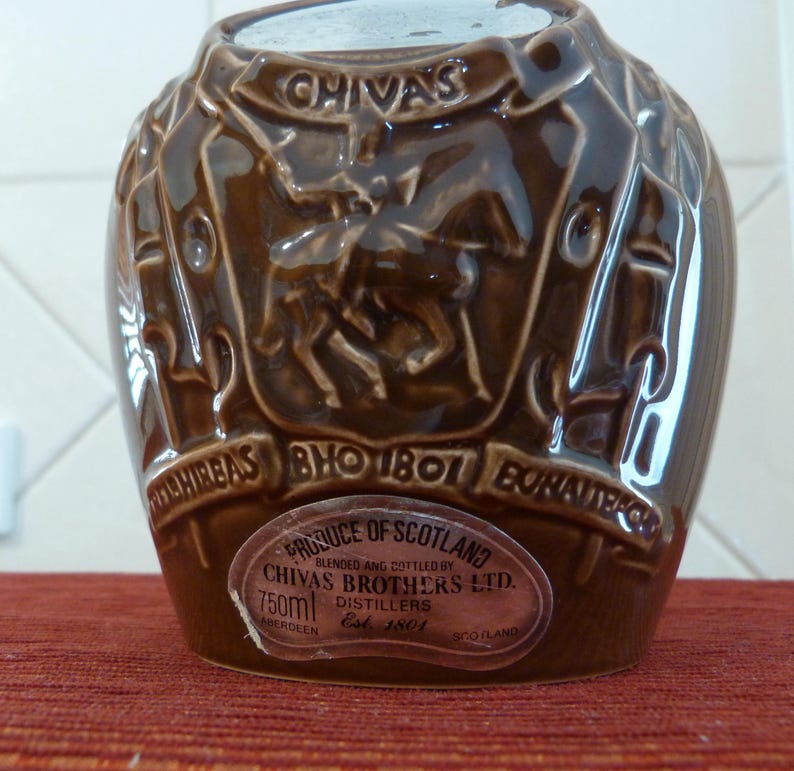 May include: A brown ceramic bottle with a label that reads "PRODUCE OF SCOTLAND BLENDED AND BOTTLED BY CHIVAS BROTHERS LTD. 750ml DISTILLERS Est. 1801 ABERDEEN SCOTLAND". The bottle has a raised design of a knight on a horse.