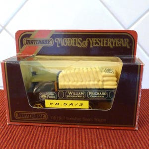 以下が含まれることがあります： オリジナルの箱に入ったMatchbox Y8 1917 Yorkshire Steam Wagonモデル。箱は濃い赤色で、金色のアクセントと「Models of Yesteryear」の文字が入っています。モデルは黒と黄色で、「William Prichard」と「Millennium Flour」の文字が入っています。