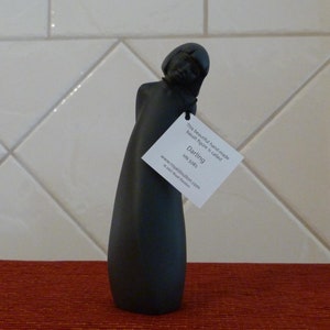 May include: Black basalt figurine of a woman with her head tilted down. The figurine is called "Darling" and is hand-made by Royal Doulton.
