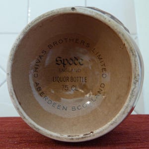 May include: Close-up of the base of a brown ceramic liquor bottle with the text "Chivas Brothers Limited Aberdeen Scotland" and "Spode England Liquor Bottle 75 cl" printed on the bottom.