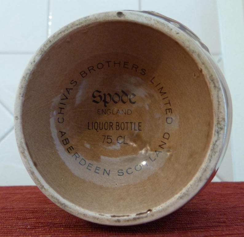 May include: Close-up of the base of a brown ceramic liquor bottle with the text "Chivas Brothers Limited Aberdeen Scotland" and "Spode England Liquor Bottle 75 cl" printed on the bottom.