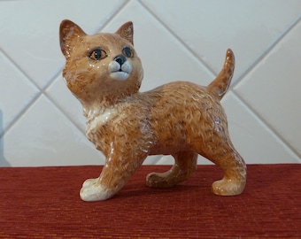 May include: A ceramic figurine of a brown and white kitten with a white chest and a fluffy tail. The kitten is standing on all fours and looking to the right.