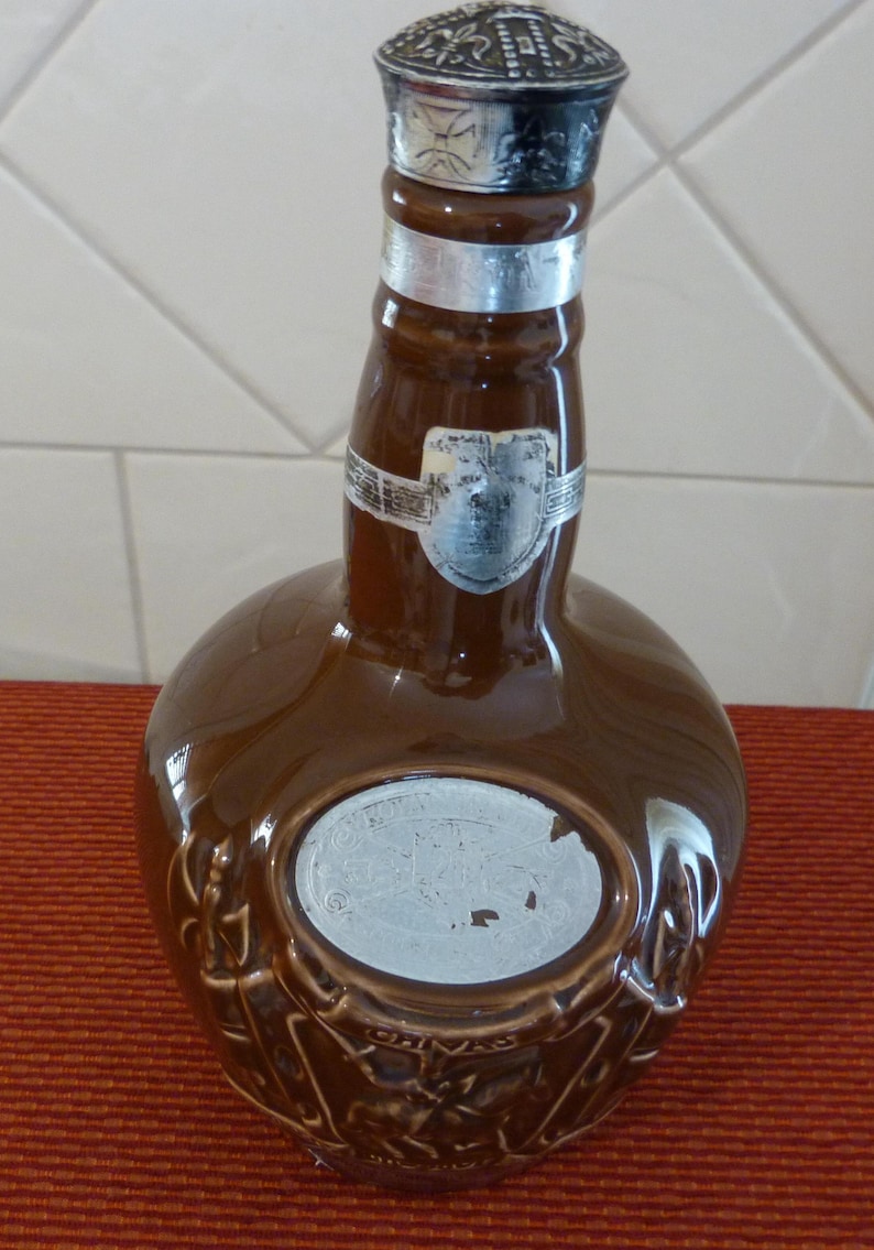 May include: A brown ceramic bottle with a silver top and a silver label that says "Chivas Regal" and "12 Years Old".