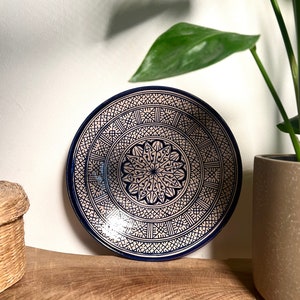 Peut inclure: Une assiette en céramique décorative avec un motif géométrique bleu et blanc. L'assiette est ronde et a un bord surélevé.