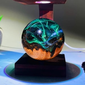 May include: A dark wood base with a green and blue resin sphere on top. The sphere has swirling patterns of green and blue resin.